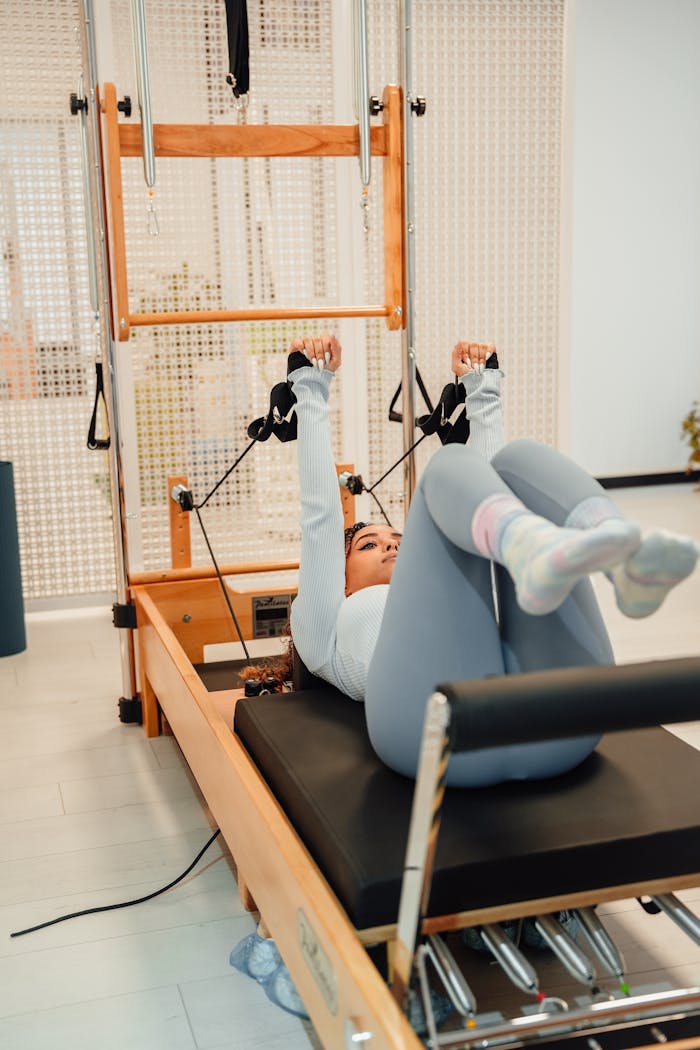 Woman in gray tracksuit performing Pilates exercises on a tower in a modern gym.